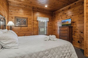 A wooden-paneled room with a bed, a television, and a window with blinds. - Mountain Movie Night in Gatlinburg (Gatlinburg)
