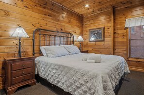 A wooden-paneled room with a bed, two bedside tables, and a window with blinds. - Mountain Movie Night in Gatlinburg (Gatlinburg)