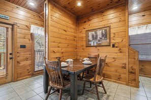 A wooden interior with a dining table set for four, surrounded by chairs, and a framed picture on the wall. - Mountain Movie Night in Gatlinburg (Gatlinburg)