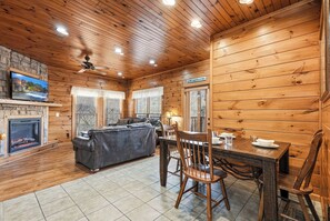 Ein gemütliches Blockhaus-Interieur mit Kamin, einer Couch, einem Esstisch mit Stühlen und einem an der Wand befestigten Fernseher.