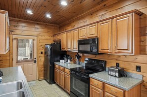 A kitchen with wooden cabinets, a refrigerator, a microwave, a stove, and a toaster. - Mountain Movie Night in Gatlinburg (Gatlinburg)