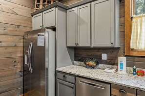 A kitchen with a stainless steel refrigerator, grey cabinets, a granite countertop, and a welcome sign. - Modern Rustic Charm in Pigeon Forge (Sevierville)