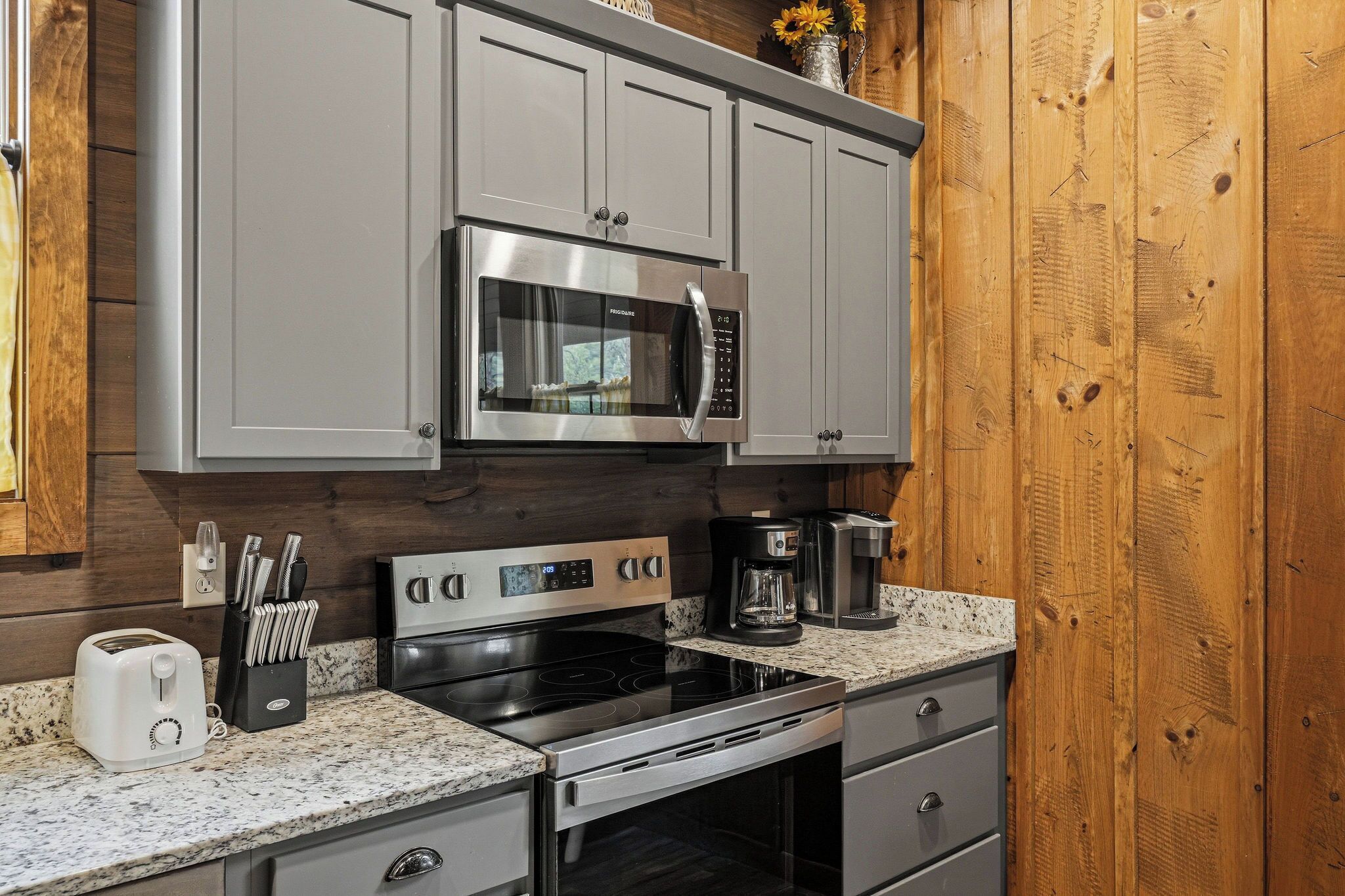 Una cocina con gabinetes grises, microondas de acero inoxidable, horno, cafetera y tostadora.