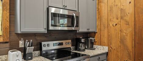 Una cocina con gabinetes grises, microondas de acero inoxidable, horno, cafetera y tostadora.