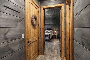 A narrow hallway with wooden walls and a door leading to a room with a bed and a nightstand. - Modern Rustic Charm in Pigeon Forge (Sevierville)