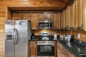 Eine Küche mit Holzausstattung und modernen, edelstahlfarbenen Geräten, darunter ein Kühlschrank, eine Mikrowelle, ein Herd und ein Backofen.