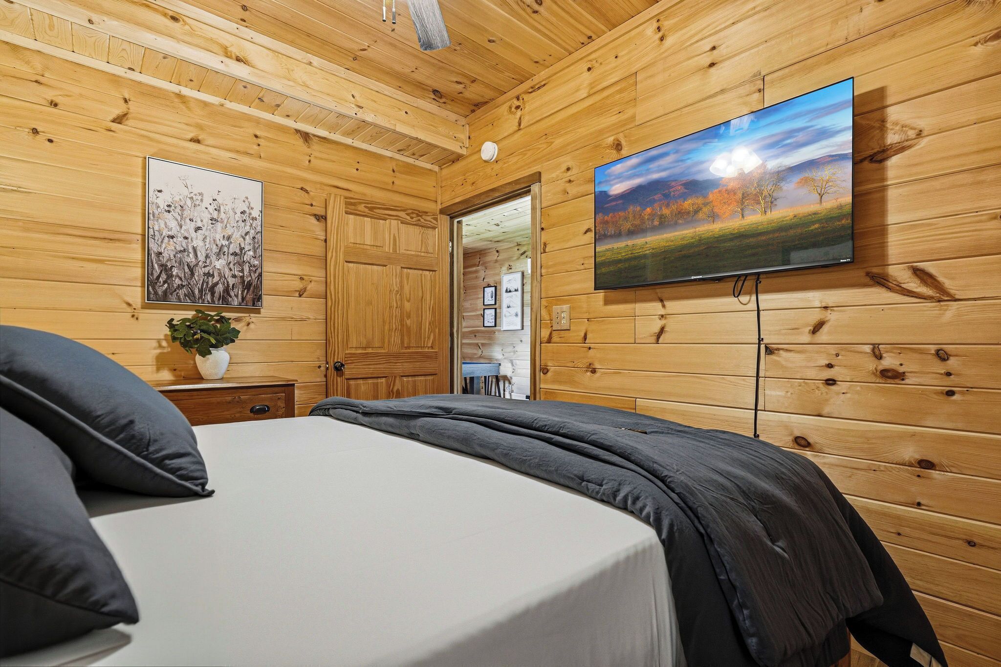 A wooden-paneled room with a bed, a television mounted on the wall, and a door leading to another room.