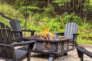 Ein Lagerfeuer mit brennenden Holzscheiten, umgeben von schwarzen Adirondack-Stühlen.