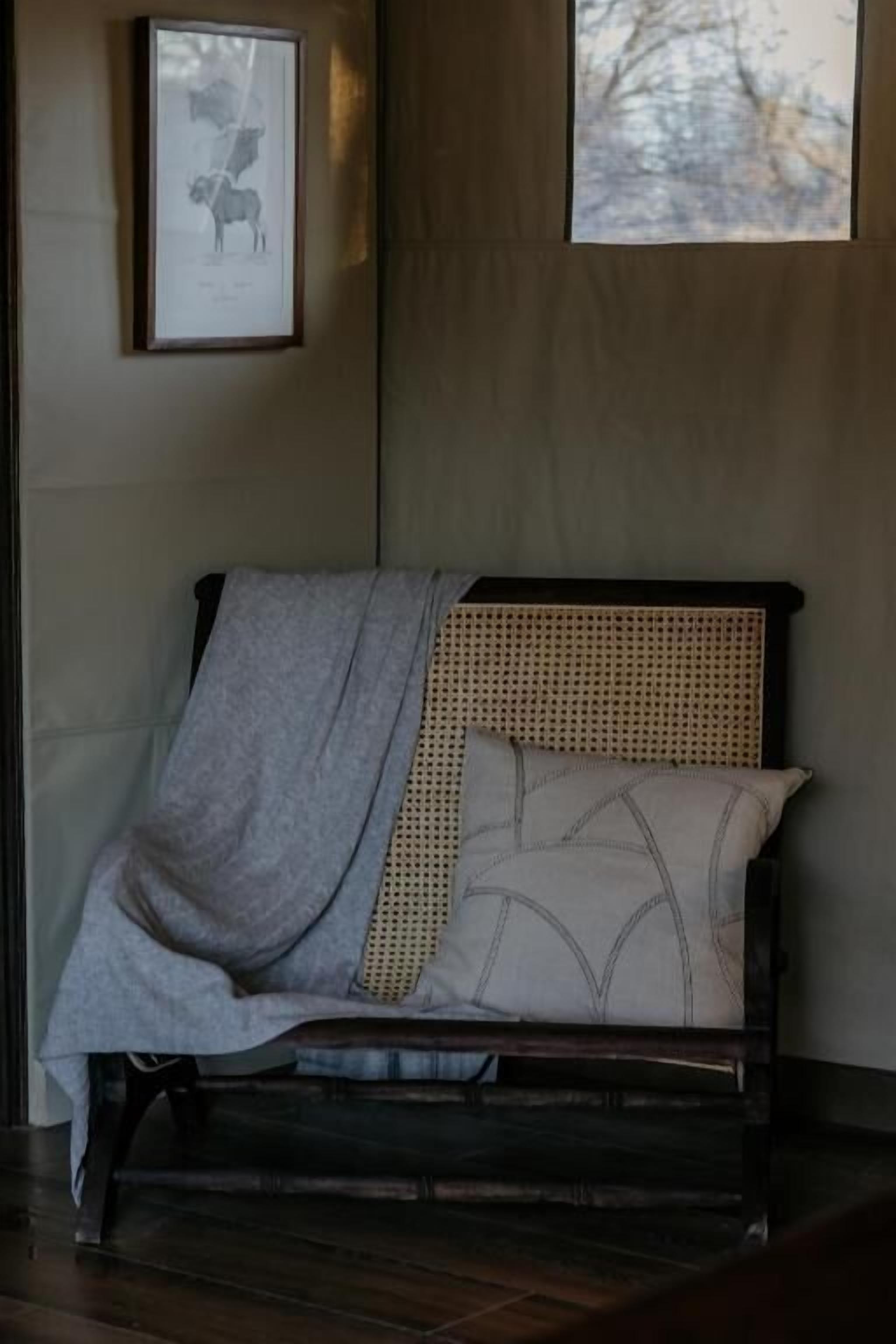 A bed with a woven headboard, a grey blanket, and patterned pillows.