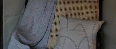 A bed with a woven headboard, a grey blanket, and patterned pillows.