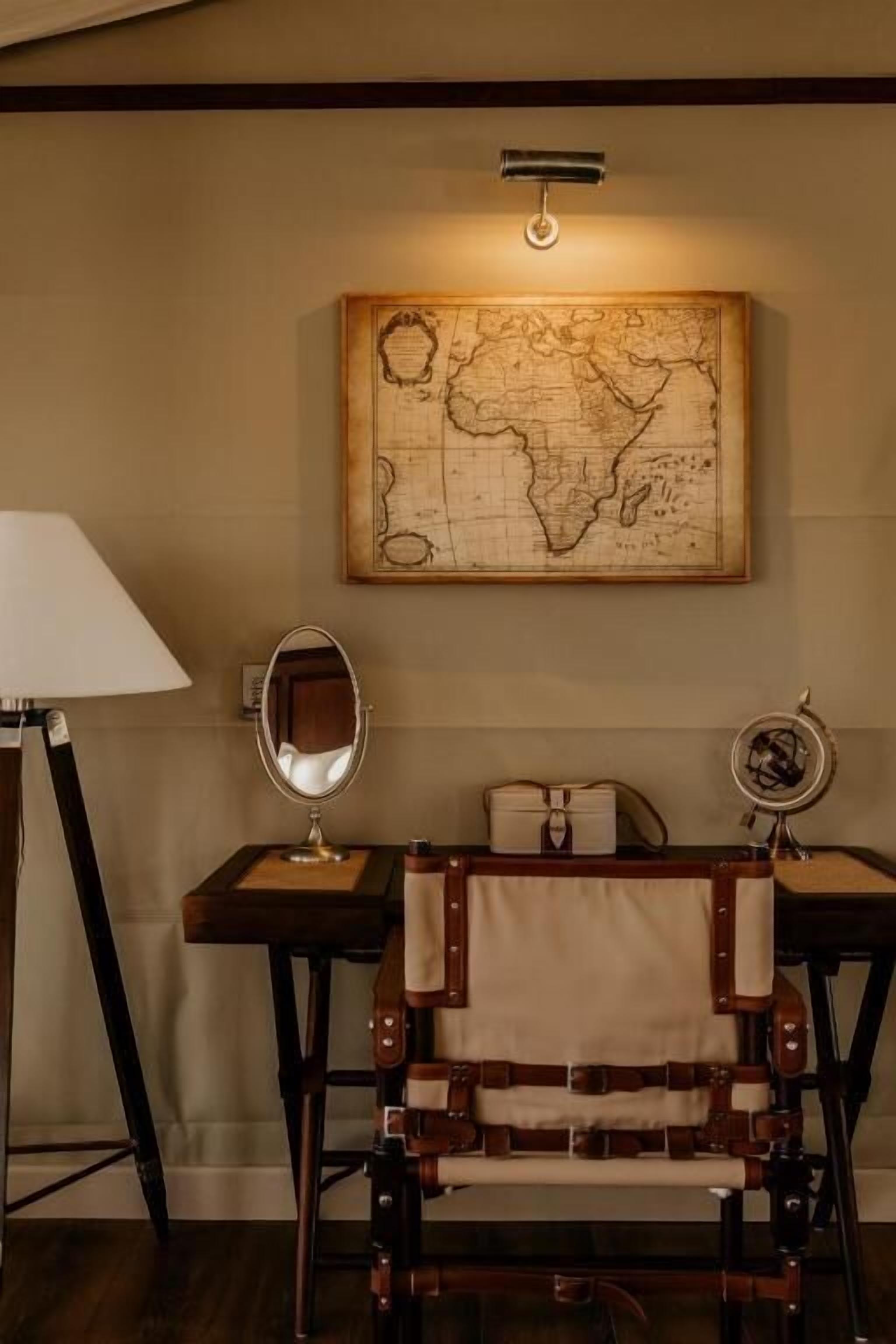 A room with a vintage-style desk, a map on the wall, and a lamp.