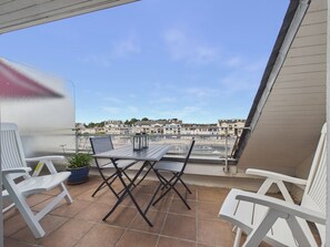 Ein Balkon mit Tisch und Stühlen, einem Blumentopf und Blick auf Gebäude über dem Wasser.