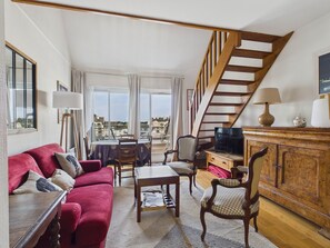 A spacious living area with a red sofa, a wooden coffee table, and a television. A staircase with wooden railings leads to an upper floor. - Port view & beach 350m away - Apartment for 4 (Le Pouliguen)