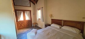 Un dormitorio con cama de madera, una mesita de noche, una pequeña mesa y una puerta con cortinas.