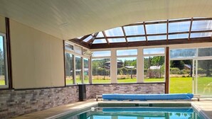 A swimming pool with a glass ceiling, surrounded by a brick wall and large windows.