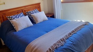 Una cama doble con cabecera de madera, una ventana con cortinas y una lámpara en la pared.