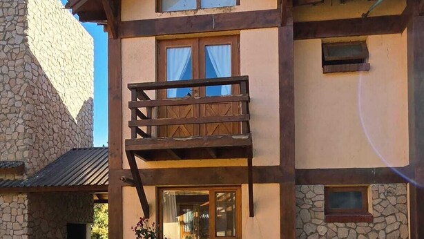 Un edificio de dos pisos con fachada de piedra, un balcón de madera y un pequeño jardín.