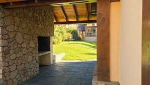 An outdoor stone fireplace with a stone wall, a wooden ceiling, and a paved patio area.