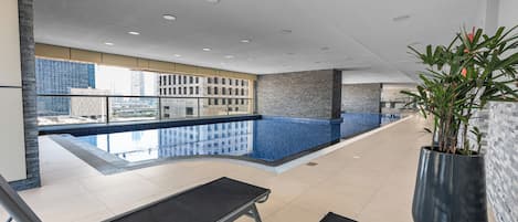 A modern indoor swimming pool with a clear view of the city skyline through large windows.