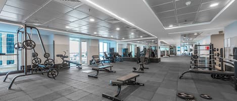Un gimnasio con diverso equipo de ejercicio, incluyendo máquinas de pesas y pesas libres, y un diseño espacioso.