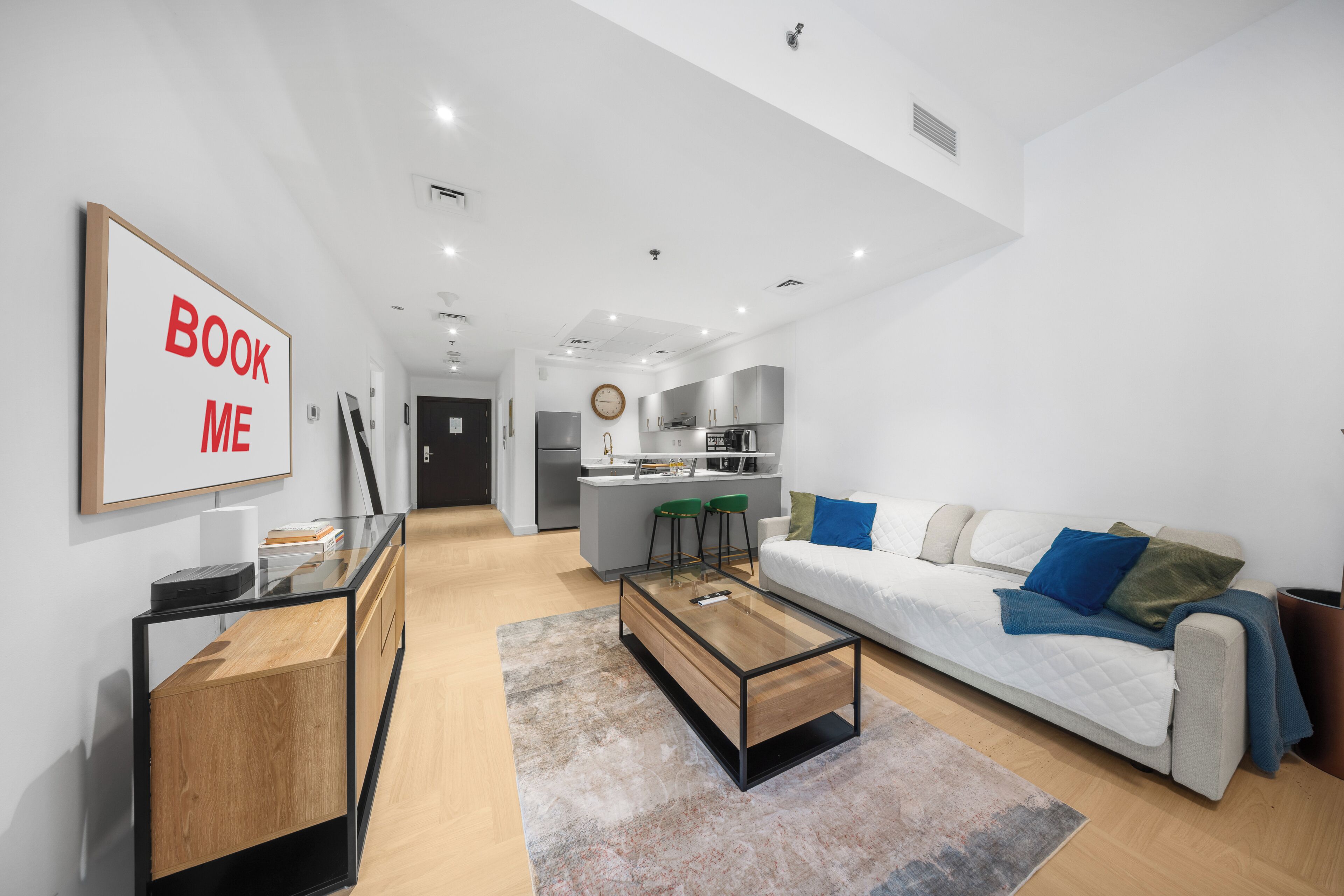 A modern living room with a sofa, coffee table, and a 'BOOK ME' sign.