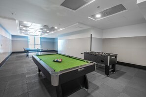 Ein Billardtisch mit grüner Spielbahn und ein Fußballtisch in einem Raum mit weißen Wänden und Fliesenboden.