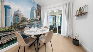 Un espace repas agrémenté d’une fresque représentant un paysage urbain, une table ronde avec des chaises et une vue sur un immeuble à travers une porte vitrée.