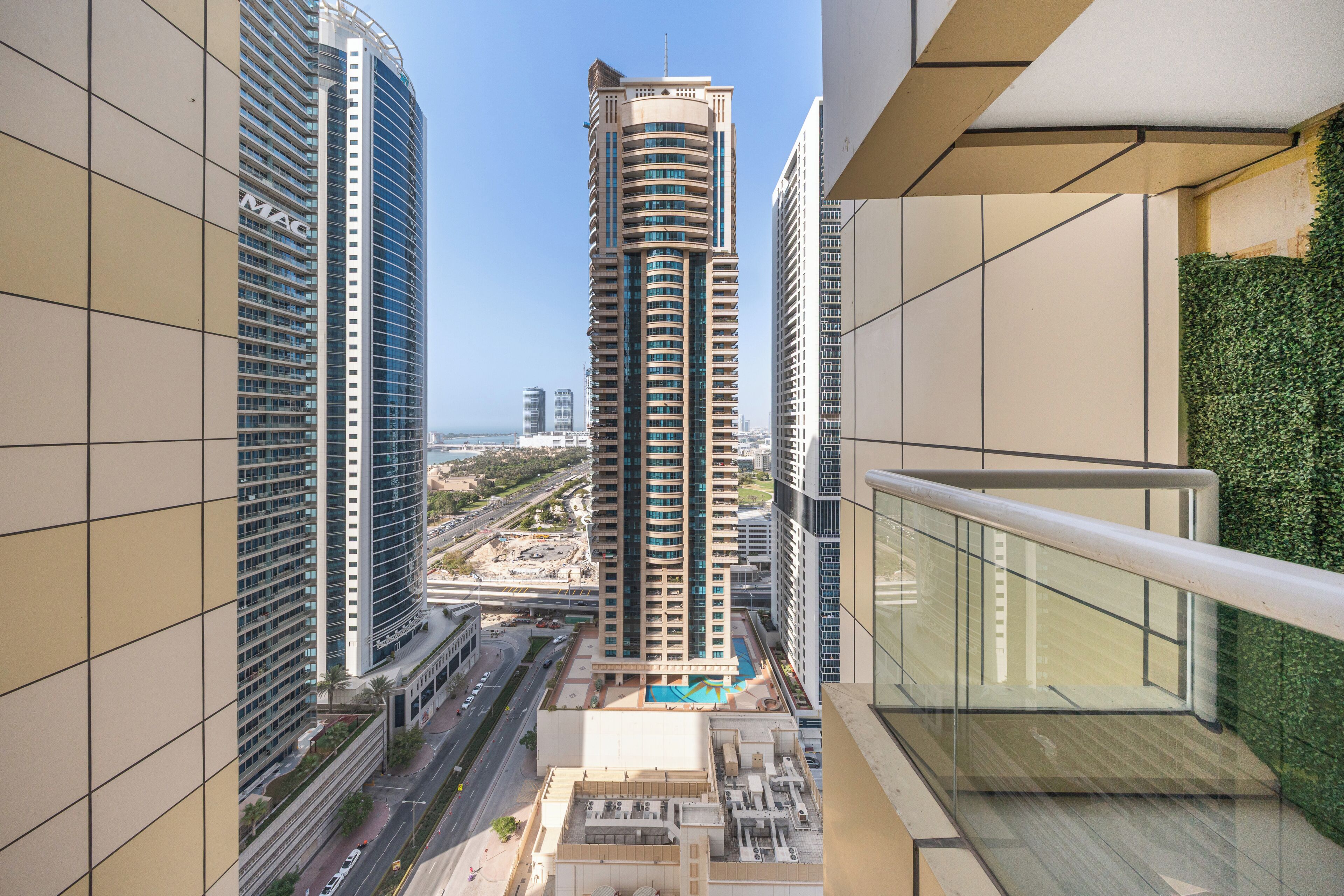 A high-rise building with a curved facade, surrounded by other tall buildings, and a view of a road and greenery below.