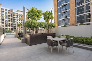 An outdoor patio area with a table and chairs, surrounded by greenery and modern buildings. - StayShort - Luxury Studio Apartment in Meydan with Balcony (Meydan)