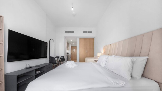 Moderni hotellihuone, jossa on suuri sänky, taulutelevisio, työpöytä ja vaatekaappi.