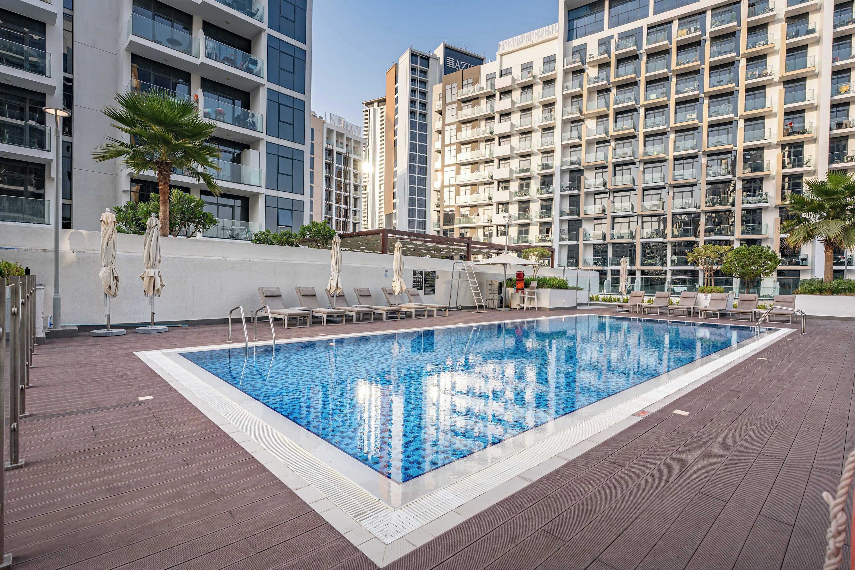 A rooftop swimming pool with lounge chairs and a view of modern buildings.