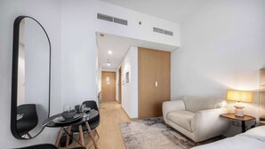 Hotellihuone, jossa on sänky, sohva, ruokapöytä tuoleineen, lamppu ja suuri peili.