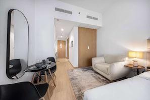 A hotel room with a bed, a sofa, a dining table with chairs, a lamp, and a large mirror. - StayShort - Luxury Studio Apartment in Meydan with Balcony (Meydan)