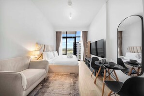 A hotel room with a bed, a sofa, a TV, a dining table with chairs, and a large window with a view. - StayShort - Luxury Studio Apartment in Meydan with Balcony (Meydan)