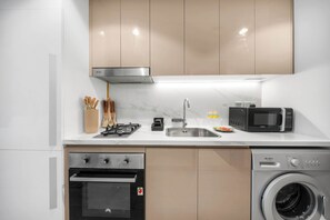 A modern kitchen with a built-in oven, microwave, and washing machine. - StayShort - Luxury Studio Apartment in Meydan with Balcony (Meydan)