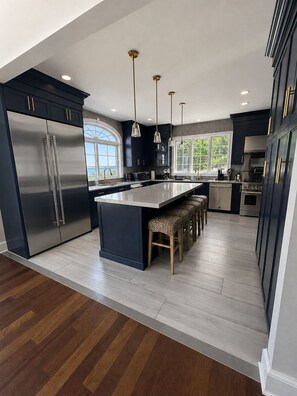A modern kitchen with dark cabinetry, stainless steel appliances, and a central island with stools.