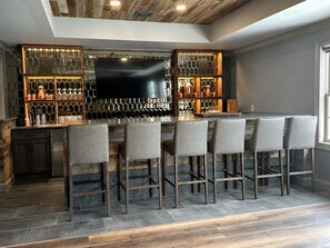 Eine Bar mit einem großen Flachbildfernseher, mehreren Barhocker und einer Holzbalkendecke.