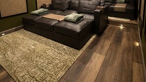 A home theater room with a sectional sofa, a carpet, and wooden flooring.