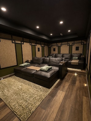 A home theater room with a sectional sofa, a carpet, and wooden flooring.