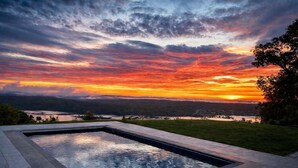A swimming pool with a view of a sunset over a lake and hills.
