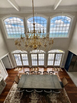 A dining room with a large table, chairs, a chandelier, and large windows with a view.