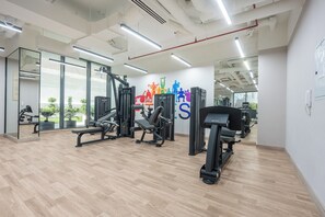 Uma academia com diversos equipamentos de exercícios, janelas amplas e uma arte motivacional na parede.