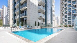 Un edificio moderno con appartamenti, una piscina, diversi balconi e un cielo sereno.