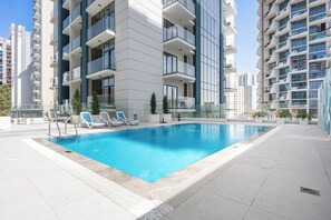 Ein modernes Apartmenthaus mit Schwimmbad, mehreren Balkonen und blauem Himmel.