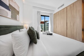 Ein Hotelzimmer mit Bett, Schrank, einem fenster mit Vorhängen und einem Bild an der Wand.