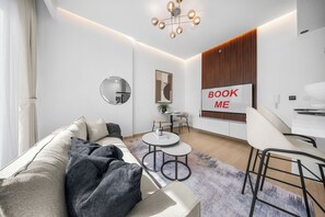 Ein modernes Wohnzimmer mit einer Couch, einem runden Spiegel, einem Couchtisch und einem Schild mit der Aufschrift 'BOOK ME' an der Wand.