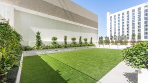 Un cortile con erba sintetica, un muro bianco e una fila di piccoli alberi.
