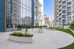 A modern building with multiple floors, large windows, and a courtyard with planters and seating. - StayShort - Amazing 1 Bedroom in JVC that Sleeps 4! (JVC)