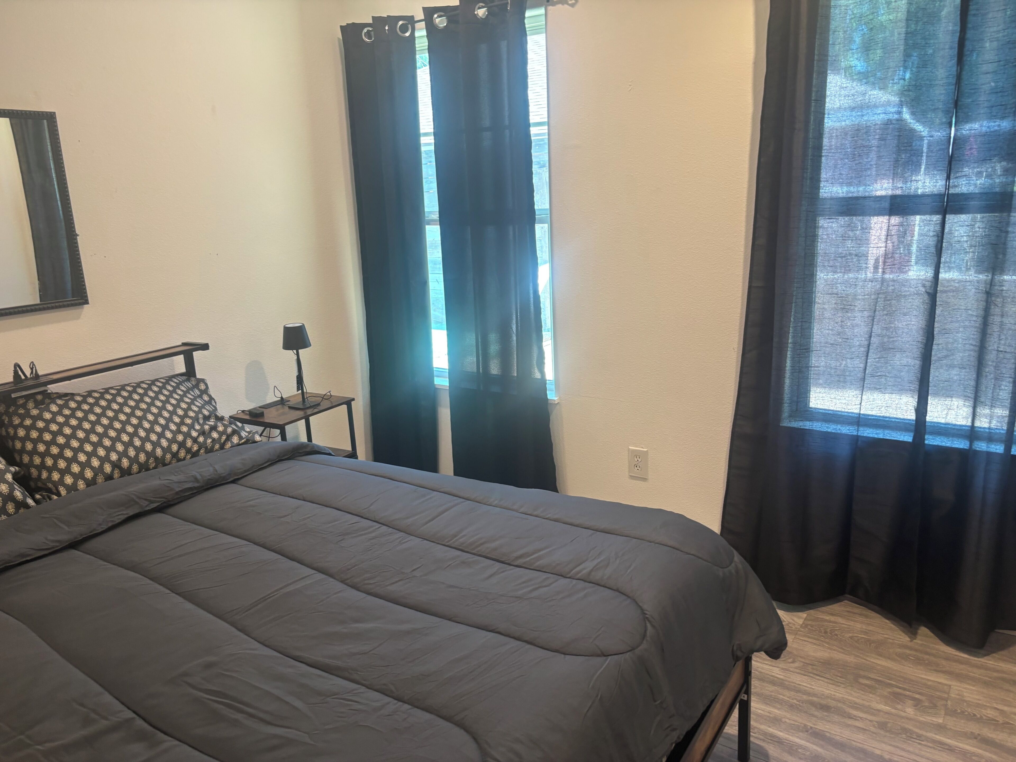 A bedroom with a bed, a nightstand, a lamp, and a window with curtains.