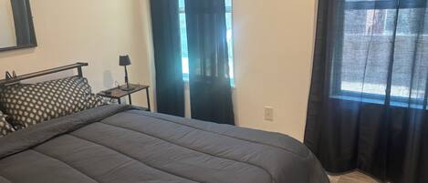A bedroom with a bed, a nightstand, a lamp, and a window with curtains.